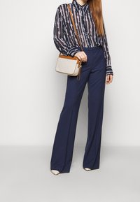 Pantaloni larghi blu abbinati a una blusa a righe bianca e nera e a una piccola borsa a tracolla beige con accenti marroni.