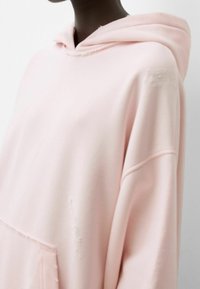 Světle růžová oversized mikina z měkké tkaniny, s přední kapsou, distressed detaily a kapucí se stahovací šňůrkou.