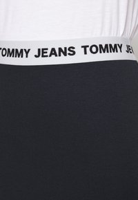 Černá elastická látka s bílým pasem, na kterém je vytištěno "TOMMY JEANS" černými písmeny. Pas má hladkou, elastickou strukturu.