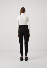 Svarta högmidjade byxor med sidfickor, tillsammans med en ribbad vit turtleneck. Skorna har nitar som dekoration.