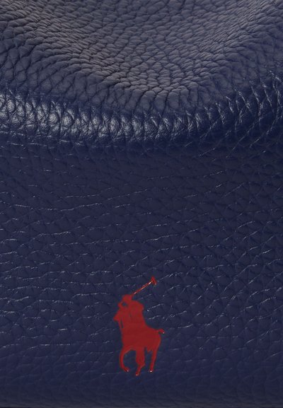 Superficie in pelle strutturata blu scuro con una piccola sagoma rossa di un giocatore di polo a cavallo che tiene un mazza.