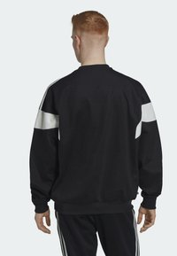 Svart sweatshirt med vita paneler på axlarna, ribbade ärmslut och nederkant, i avslappnad passform och mjukt material.