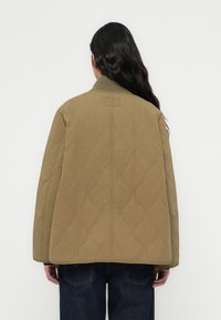 Πουπουλένιο σακάκι σε ελιά χρώμα με ριμπ γιακά και στρογγυλεμένη άκρη, διακοσμημένο με υφή. Φορεμένο πάνω από σκούρο τζιν.