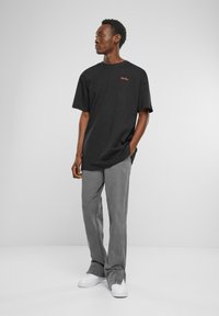 Sort bomulds T-shirt med korte ærmer og rød broderet tekst, parret med grå vide bukser og hvide sneakers.