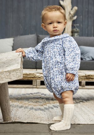 Romper pour bébé à motifs floraux bleus avec des manches bouffantes et un corsage froncé, associé à des chaussettes hautes crème avec un motif en dentelle.
