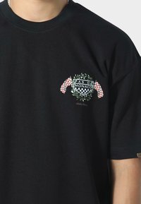 Sort bomulds T-shirt med et broderet skjold med "PAS DE MONACO", omgivet af laurbærblade og ternede flag. Korte ærmer.