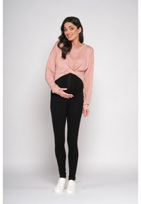 Haut à manches longues rose avec un design à l'avant torsadé, associé à un legging noir et des baskets blanches. Texture lisse, silhouette ajustée et style décontracté.