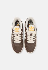 Bruna lädersneakers med krämfärgade snören och tre vita ränder. Har en vadderad krage och en mönstrad innersula. Adidas-logotyp på tungan.