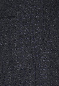 Gros plan sur un tissu texturé sombre avec un motif tissé comportant de petites boucles et un léger éclat dans des tons marine et noir.