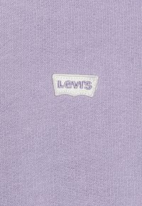 Tessuto lavorato a maglia viola con una toppa bianca del logo Levi's con lettering viola, posizionata centralmente sul capo.