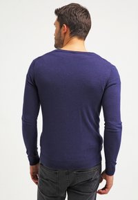 Mörkblå stickad tröja med långa ärmar, ribbade manschetter och rund halsringning, med en slät textur och figurnära design.