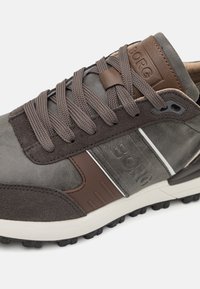 Grijze synthetische schoenen met bruin leren accenten, gestructureerde veters en een rubberen buitenzool. Voorzien van branding aan de zijkant en kenmerkende ontwerp lijnen.