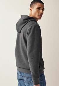 Grå tekstureret hættejakke med et vævet mønster, der har en hætte og ribbede manchetter, parret med blå jeans.