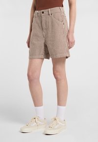 Pantalones cortos a rayas marrones y blancas con cintura alta, bolsillos frontales y corte recto. Combinados con zapatillas beige y calcetines blancos de caña baja.