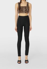 Czarne spodnie z wysokim stanem o slim fit, z przeszyciami z przodu. W zestawie z krótkim topem w panterkę. Buty to czarne klapki na obcasie.