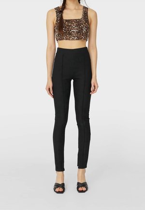 Pantalons noirs taille haute à coupe ajustée, avec des coutures avant. Associés à un crop top à imprimé léopard. Les chaussures sont des mules noires à talons.