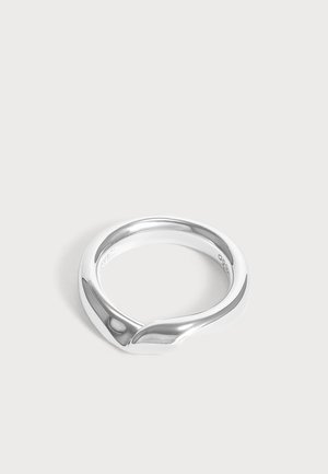 Anillo plateado liso con un diseño moderno y curvado que forma una sutil forma de onda sobre un fondo claro y sencillo.