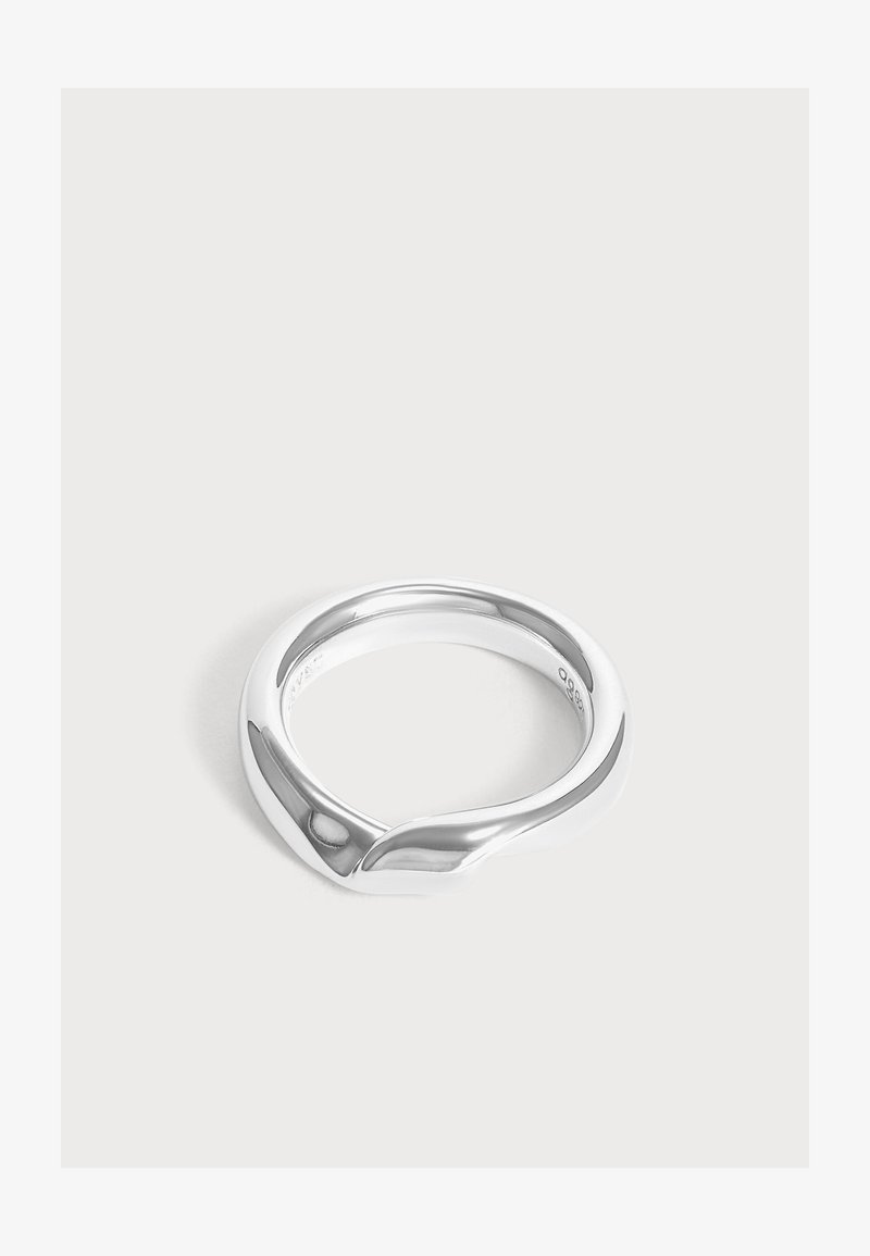 Bague en argent lisse avec un design moderne et incurvé formant une forme subtile de vague sur un fond clair uni.