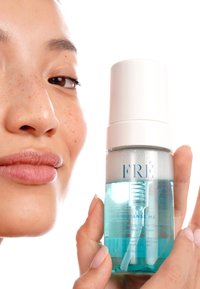 Schuimende micellaire reiniger in een heldere, ronde fles met een witte pomp. Het etiket heeft blauwe letters, de vloeistof is lichtblauw en een gestructureerd patroon is zichtbaar.