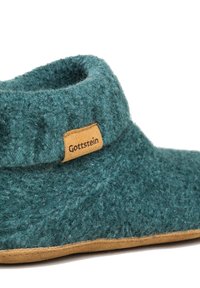 Pantofole teal con taglio basso e texture morbida. Presenta un'etichetta in pelle beige con il logo "Gottstein". Sottopiede in suede per presa e comfort.