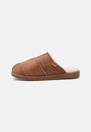 Chausson marron à enfiler avec doublure douce en polaire blanche, dessus cousu et semelle plate conçue pour le confort en intérieur.