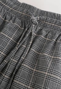 Szara tkanina w kratę o fakturowanej powierzchni z czarnymi, białymi i beżowymi wzorami. Zawiera elastyczną talię z wiązaniem.