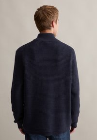 Granatowy sweter dziany o teksturowanym wykończeniu, z kołnierzem stójkowym i ściągaczami na mankietach. Luźny krój, długie rękawy i minimalistyczne detale.
