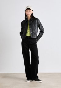 Svart läderkort jacka med två framfickor, kombinerad med en grön skjorta och svarta vida byxor. Svarta sneakers med vit sula, beige keps.