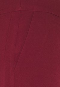 Gros plan sur un tissu bordeaux, surface texturée avec des coutures visibles et des panneaux angulaires, offrant une couleur riche et un design structuré.