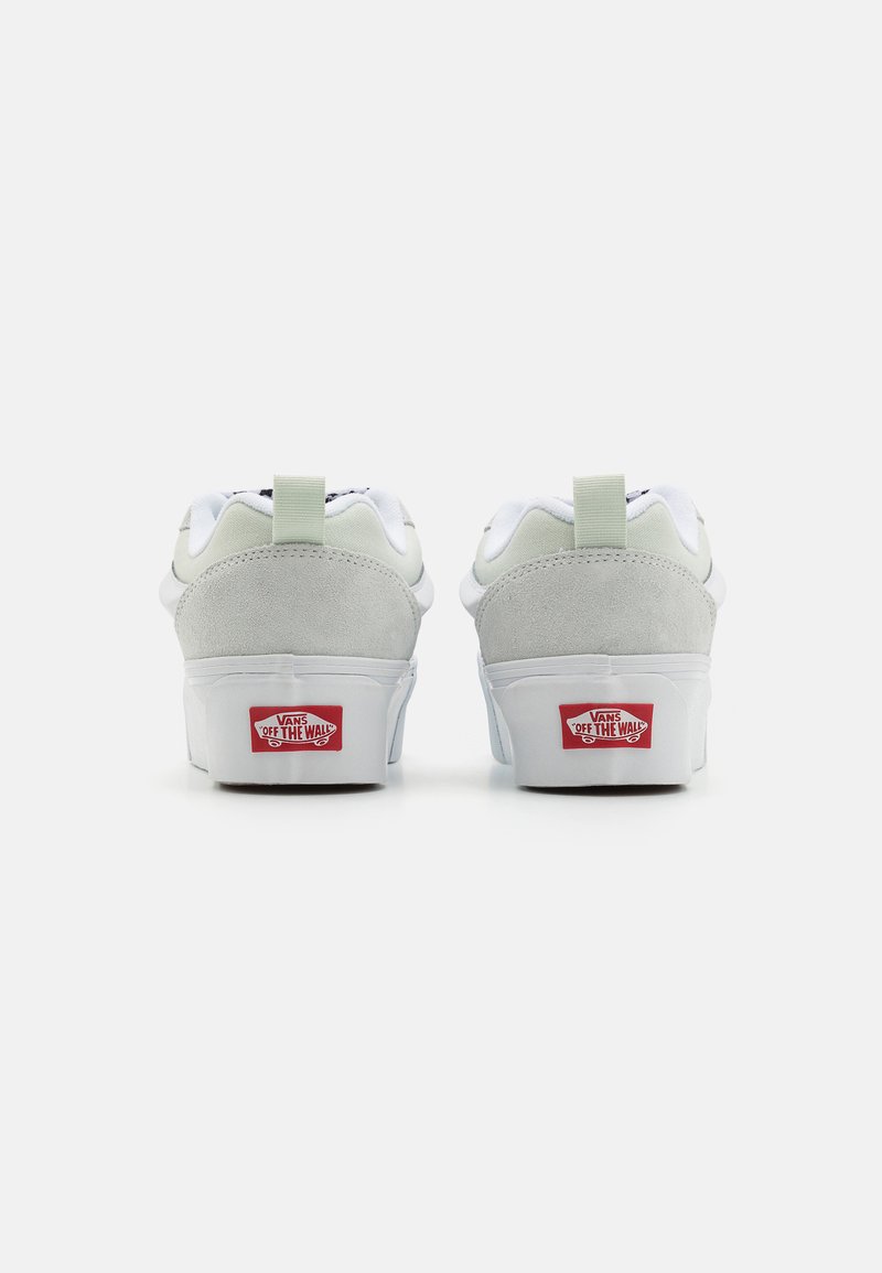 Zapatillas de ante blancas y grises con un cuello acolchado, que presentan una pestaña en el talón de color verde y el logotipo rojo "Off the Wall" en la suela.