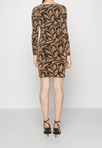 Robe noire à manches longues, ornée d'un motif de feuilles dorées. Le tissu a une finition texturée. Portée avec des talons à lanières noirs.