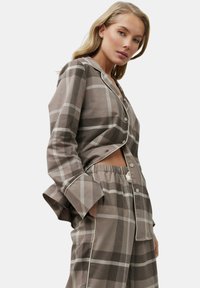 Geruit pyjamaset met een bovenstuk met knopen en een broek met elastische tailleband. Kleuren zijn beige en bruin met witte accenten. Gemaakt van katoen.