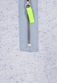 Sudadera de color lila claro con cremallera, con un patrón texturizado, que presenta una cremallera de metal plateado y una lengüeta de tirón de color verde brillante.