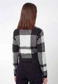 Sort og hvid ternet cropped sweater med et struktureret strikkemønster, lange ærmer og ribkant forneden. Båret med sorte bukser.