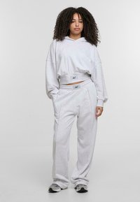 Hoodie grigio chiaro a vita corta con maniche oversize e cappuccio con cordino, abbinato a pantaloni della tuta larghi coordinati con tasche laterali.
