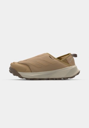 Scarpe slip-on in materiale sintetico color marrone. Presentano una suola testurizzata, un design minimal con pannelli laterali e una linguetta sul tallone.