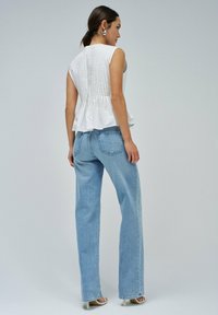 Top blanco sin mangas con cuerpo texturizado y diseño de peplum, combinado con jeans de pierna ancha azul claro. Sandalias de tacón en tonos neutros.