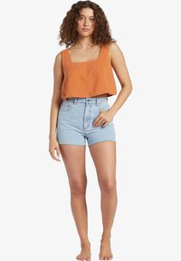 Rust-colored cropped tank top with square neckline and textured fabric, paired with high-waisted light blue denim shorts with frayed hem.