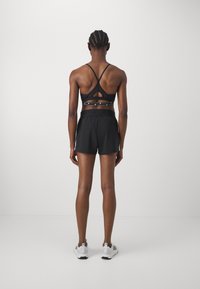 Svart sportbh med ett korsat ryggdesign och ett nyckelhålsutsnitt, tillsammans med svarta shorts. Båda plaggen har en mjuk yta.