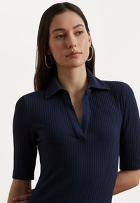 Marinblå ribbade polo-shirt med korta ärmar och en liten krage, med en knapplist vid halsöppningen. Slät textur med vertikala linjer.