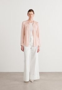 Blusa button-up rosa chiaro con dettaglio di scollatura arricciata, abbinata a pantaloni bianchi a gamba larga con vita alta; tessuto liscio e vestibilità sartoriale.