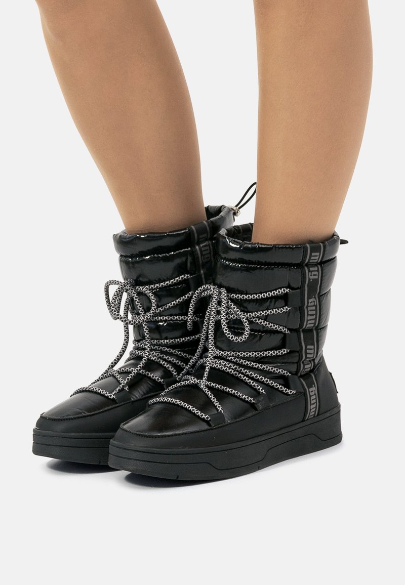 Botas de tobillo acolchadas negras con acabado brillante, que presentan suelas gruesas negras, cordones grises gruesos y parte superior con cordón ajustable para un ajuste personalizable.