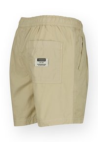 Beige šortky vyrobené z lehké tkaniny. Mají elastický pas, boční kapsu a zadní nášivkovou kapsu s označením značky. Hladká textura.