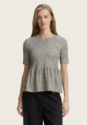 Schwarz-weiß gepunktetes Peplum-Top aus leichtem Stoff, mit kurzen Ärmeln und rundem Ausschnitt. Kombiniert mit schwarzen Hosen.