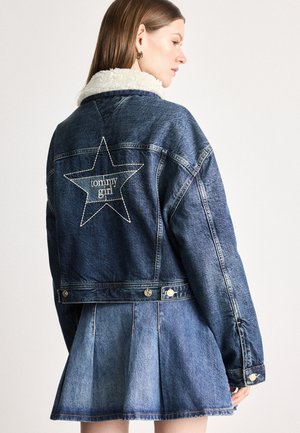 Veste en denim avec un col en fausse fourrure, présentant une étoile blanche et le logo "tommy girl" brodé à l'arrière. Couleur bleu clair et bleu foncé.