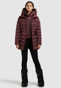 Bordo puhovka z visokim ovratnikom in kapuco; ima vodoravno šivanje, dva bočna žepa in zadrge; kombinirana s črnimi pajkicami in škornji.