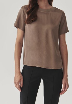 Short-sleeve brown silk blouse with a round neckline and a smooth, slightly glossy texture. Paired with black tailored pants.
