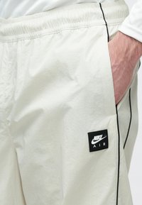 Ανοιχτό μπεζ σορτς με ελαστική μέση, πλαϊνές τσέπες, μαύρες ραφές και μαύρο, με επώνυμο λογότυπο Nike Air, επιπρόσθετο στην αριστερή πλευρά.