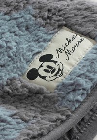 Tejido peludo gris y azul con una textura suave, que presenta una etiqueta de Mickey Mouse cosida en crema. Forma de tamaño mediano.