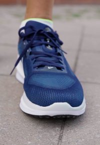 Scarpa sportiva di colore blu navy con tomaia in rete, suola bianca a contrasto e lacci scuri. Design testurizzato con perforazioni per la traspirabilità.